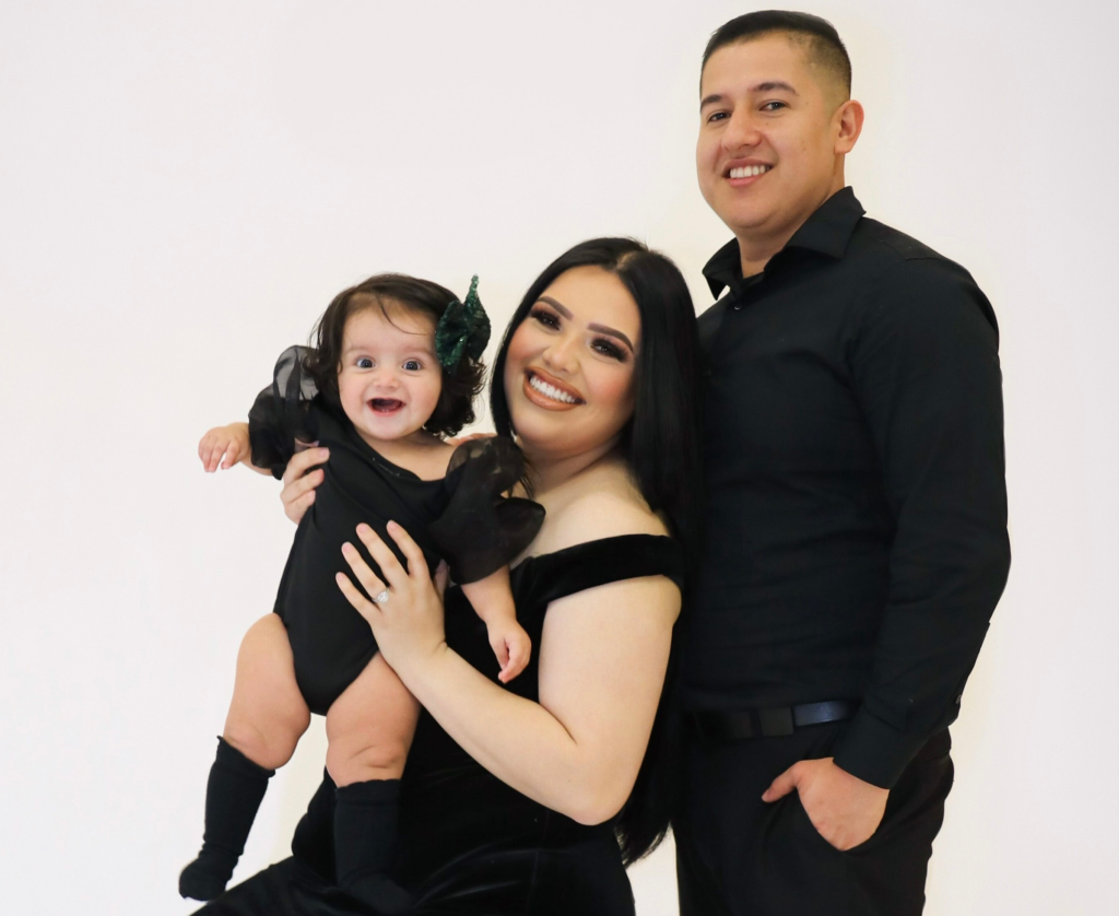 Karina Garcia poses with husband Raul Aguilar and daughter Mia Violeta against a grey background
