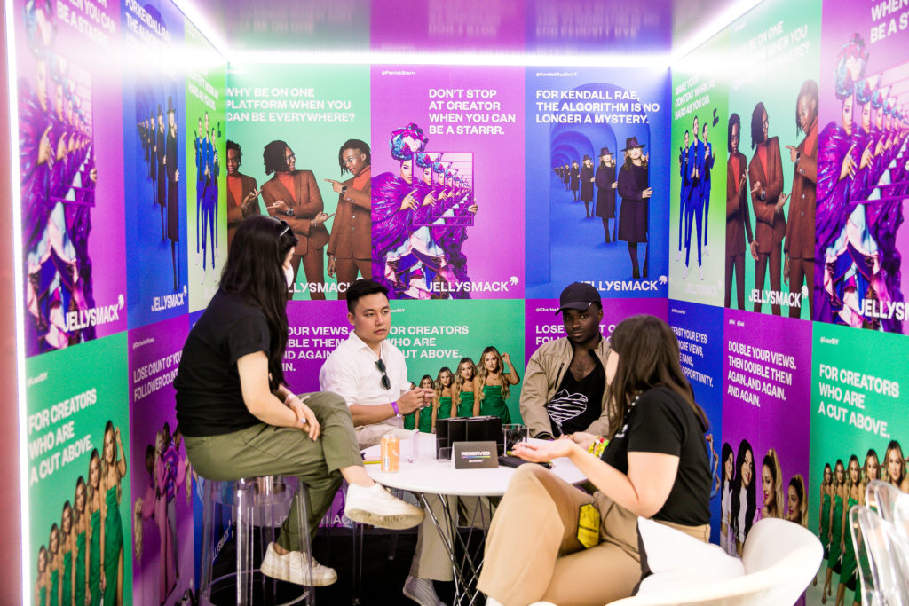 Four people sitting at a table discussing the creator economy in a room full of colorful posters at the Jellysmack Creator Lounge at VidCon 2022