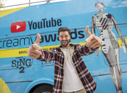 Creator Jeff Whitek makes an excited gesture while standing if front of the blue YouTube Streamy Awards bus
