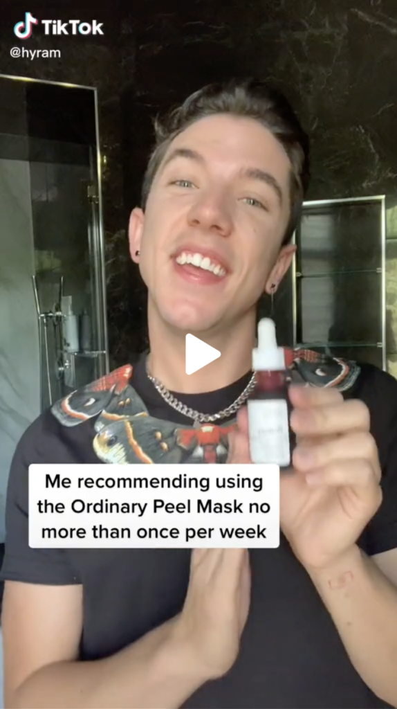 Portrait of Hyram Yarbro holding a bottle of skin care in a bathroom with text "Me recommending using the Ordinary Peel Mask no more than once per week"