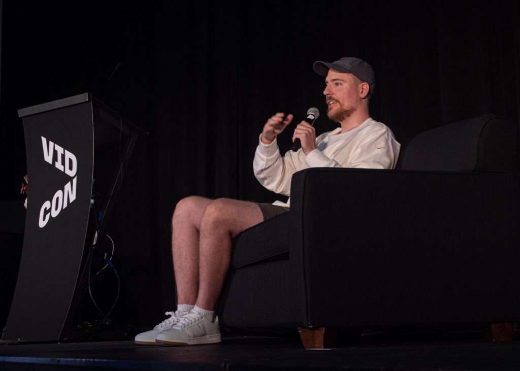 Creator MrBeast sitting down on stage at VidCon holding a microphone speaking to an audience