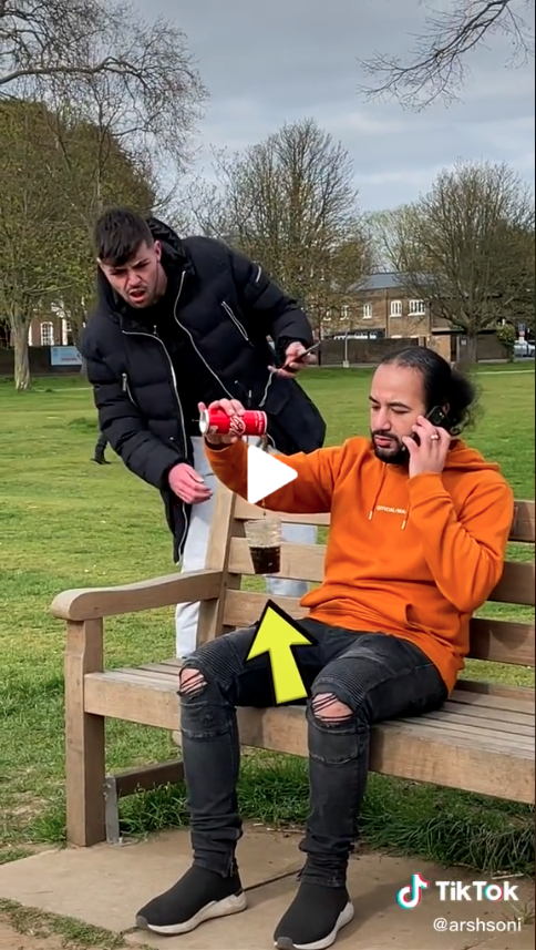 Creator Arshdeep Soni sitting outside on a park bench pouring a can of Coke into a floating glass while an onlooker is amazed