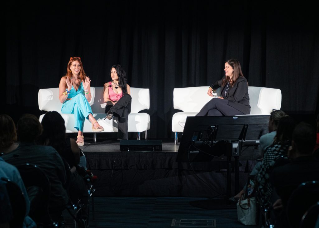 Creators Charlotte Dobre and Niki DeMartino sitting on a white couch on stage chatting with Jellysmack's Cat Valdes at VidCon 2022