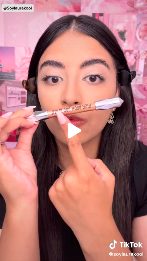 Creator SoyLauraKool pointing to a concealer makeup brush while looking into the camera on a pink background