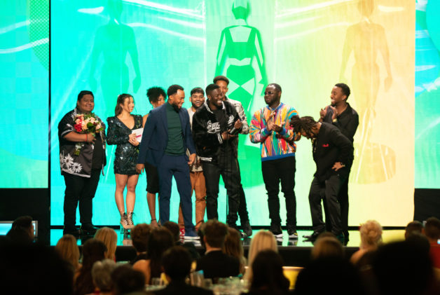 Group of men accept an award on stage with green background.