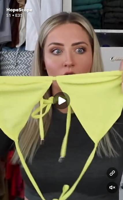 Creator HopeScope looking wide eyed while holding up a yellow triangle bikini top in a closet