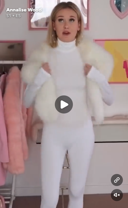 Creator Annalise Wood wearing a Kyle Jenner-inspired outfit of a white long-sleeve catsuit and faux fur shawl in a bedroom