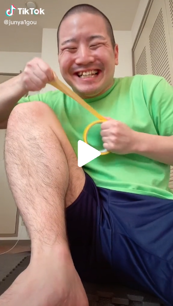 Creator Junya sitting smiling in a green t-shirt and blue shorts pulling out a yellow piece of tape