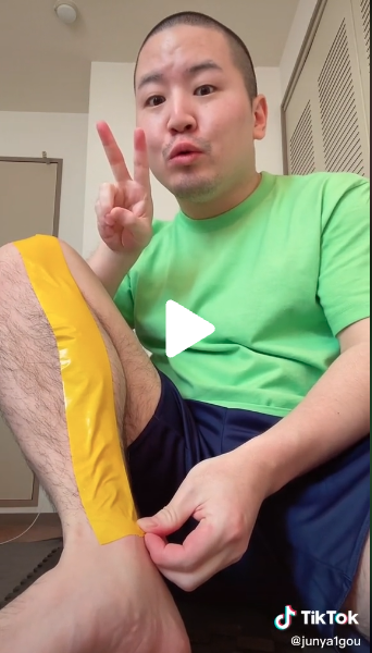 Creator Junya sitting in a green t-shirt and blue shorts holding up two fingers as he counts down to tearing yellow tape off of his leg