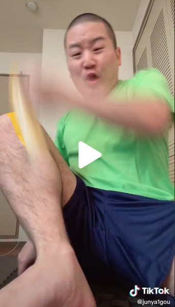 Creator Junya sitting in a green t-shirt and blue shorts ripping off a piece of yellow tape from his leg