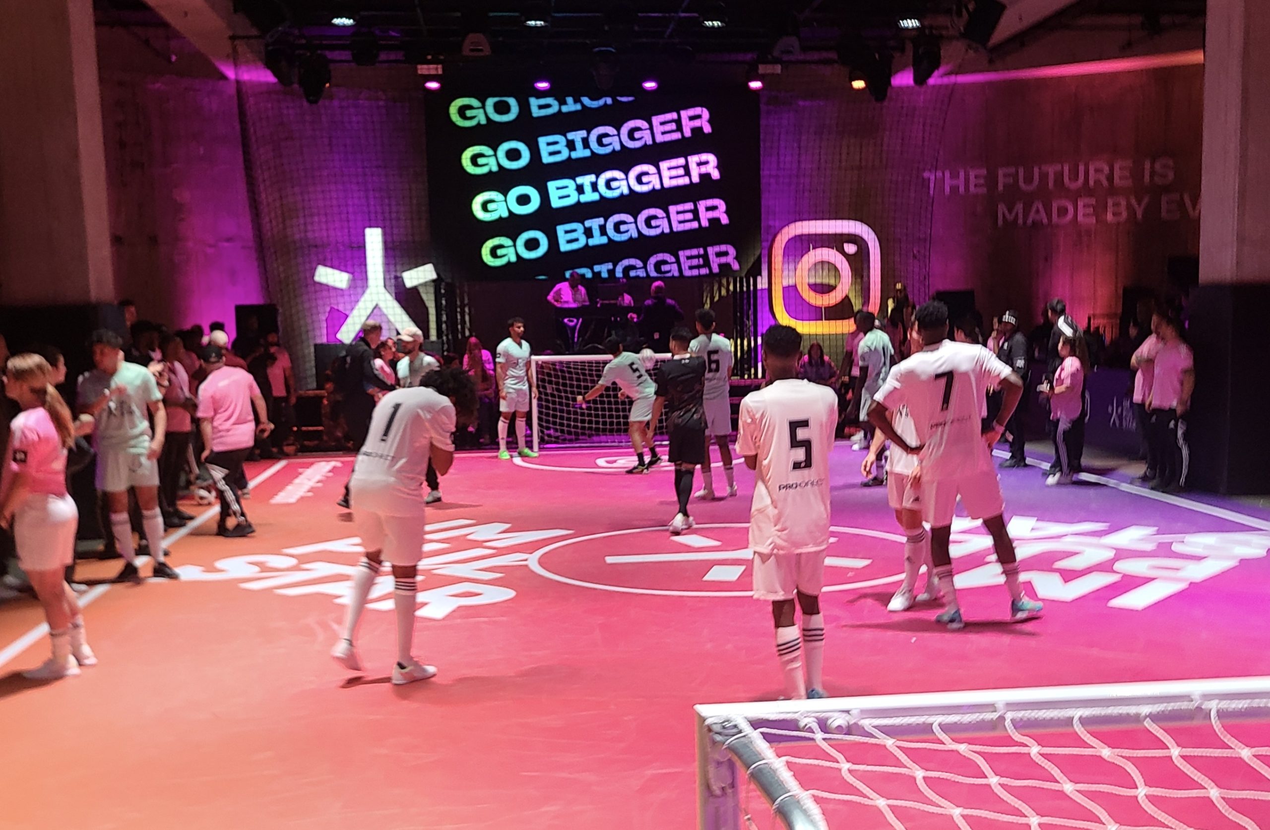 Soccer players on a pink and orange indoor pitch with an Instagram logo and Jellysmack's Go Bigger tagline in the background