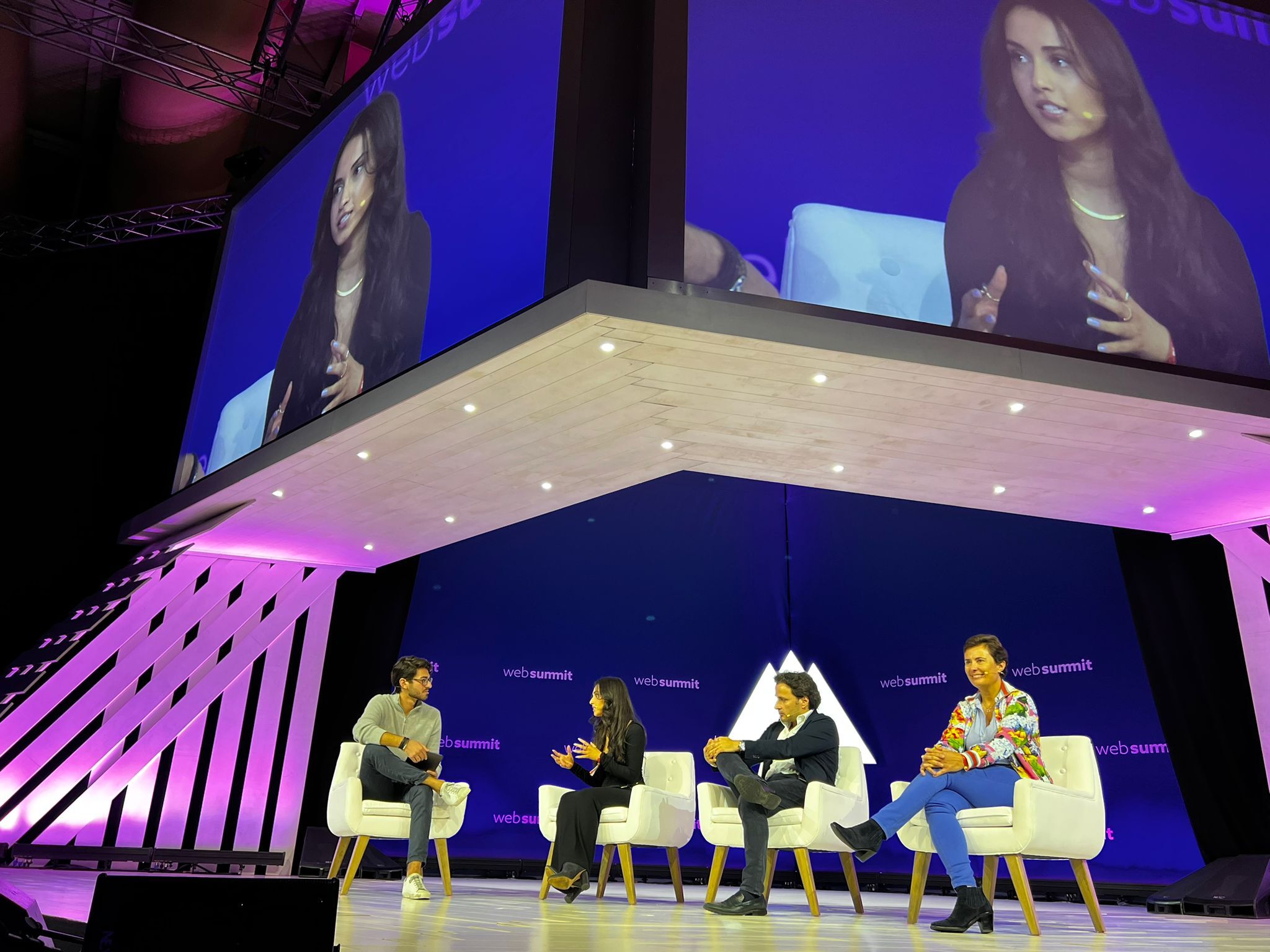 Four panelists sit on stage beneath a large screen that shows a female panelist speaking.