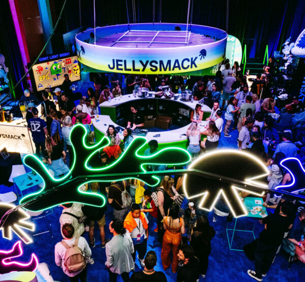 Birds eye view of Jellysmack VidCon lounge featuring neon lights, colorful signage and a crowd of people