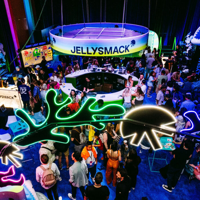 Birds eye view of Jellysmack VidCon lounge featuring neon lights, colorful signage and a crowd of people